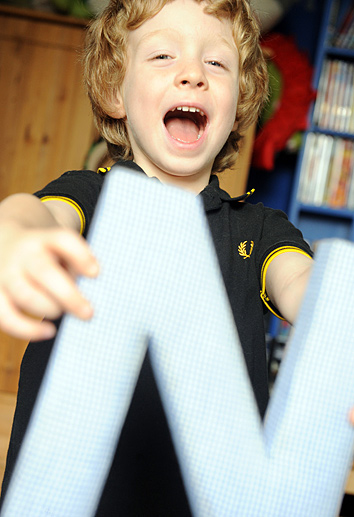 A happy boy holds a letter from his name and laughs