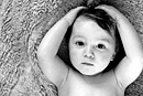 A toddler lies on a rug and holds his head, black and white image