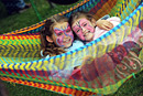 Two girls with their faces painted lie in a brightly coloured hammock