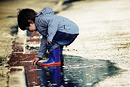 A toddler plays in a puddle in his wellington boots