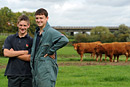 Two young farmers pose in fron of some cows