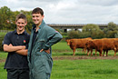 Two young farmers pose in fron of some cows