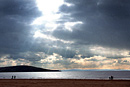 The sun breaking out from behind the clouds over the beach