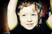 A boy raises his arms over his head while smiling and playing