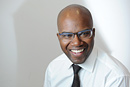 A portrait of a man wearing glasses against a white backdrop